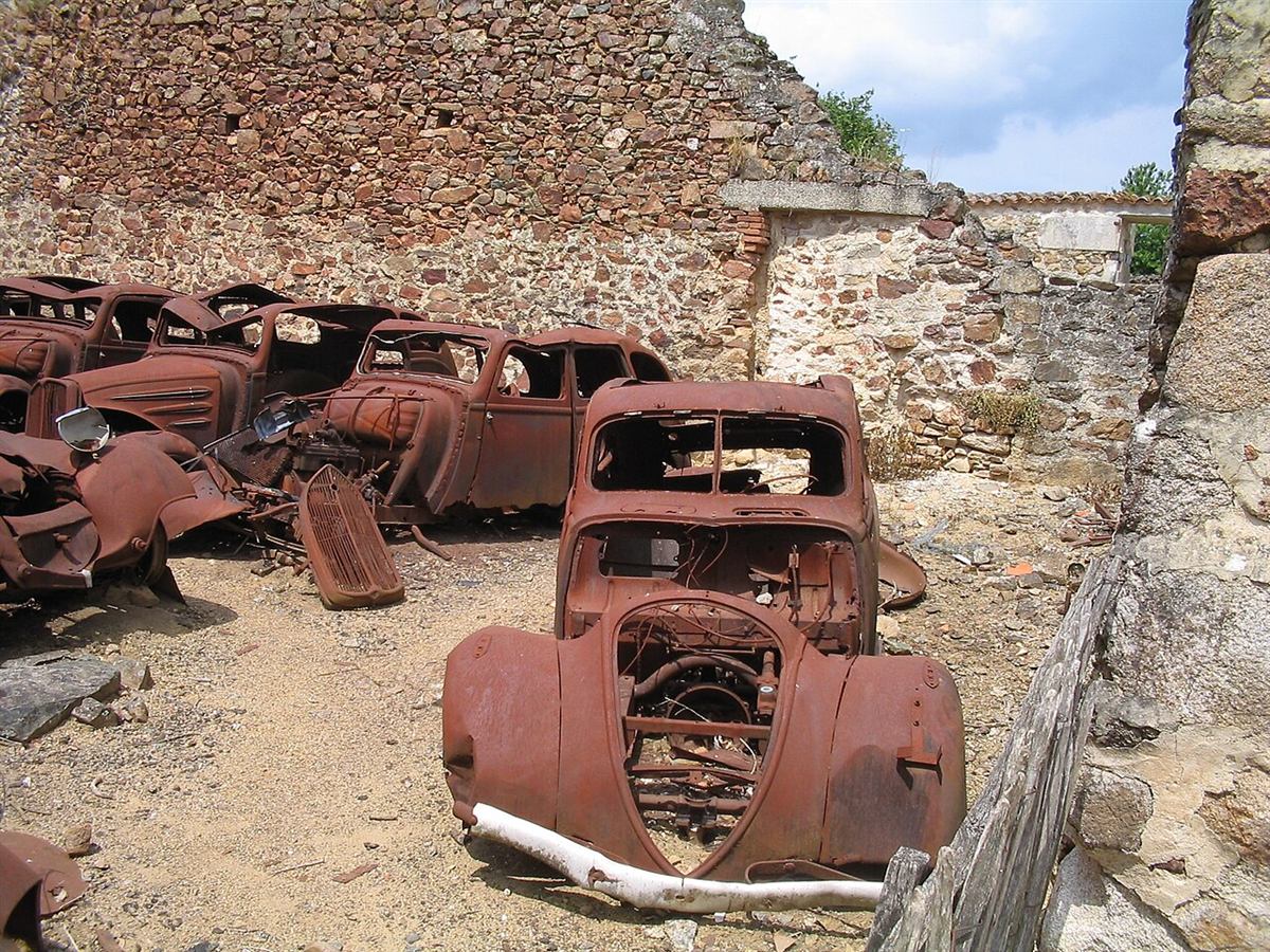 Rustne bilvrak fra 1944 som fortsatt står mellom ruinene i Oradour-sur-Glane