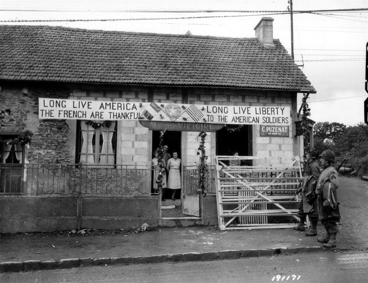 Hus i Le Molay-Littry i 1944 med bannere som takker de amerikanske soldatene
